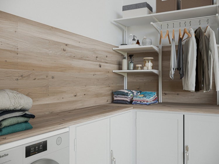 Heller Wäscheraum mit Wandpaneelen in Holzoptik, weißem Regalsystem mit Kleidung und weißen Unterschränken mit Holz-Arbeitsplatte.