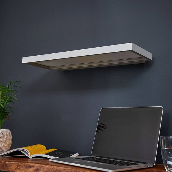 Schlanke, weiße LED-Wandleuchte über einem organisierten Arbeitsplatz mit Holzschreibtisch, Laptop und Pflanze an einer dunklen Wand.