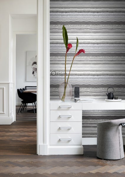 Szene mit gemusterter Tapete, Kommode, Vase mit Blumen und Stuhl in einem hellen Raum.