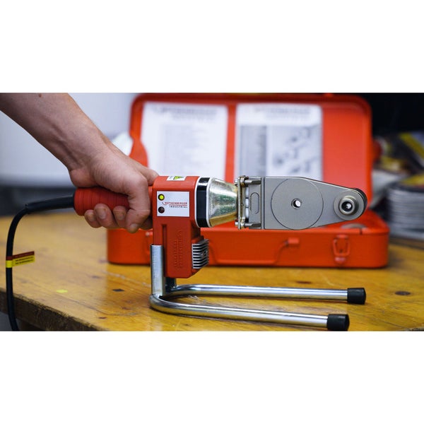 Strukturierter Wohnbereich mit grauem Lammfell auf Polstersessel, dickem Schlingen-Teppich und Strick-Pouf vor einer Ziegelwand.