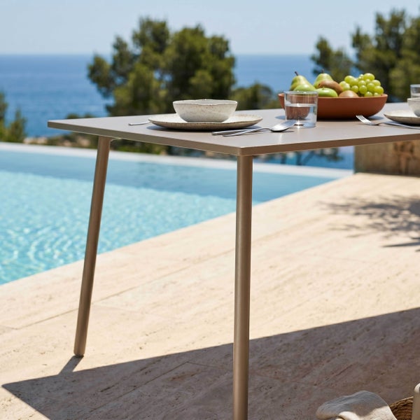 Moderner Gartentisch aus Metall auf einer Terrasse am Pool, gedeckt mit Geschirr und einer Obstschale mit Blick auf das Meer.