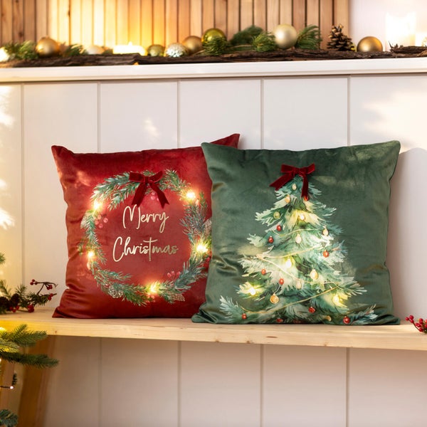 Zwei quadratische Weihnachtskissen mit integrierter LED Beleuchtung, bedruckt mit einem Weihnachtskranz und einem Weihnachtsbaum Motiv.