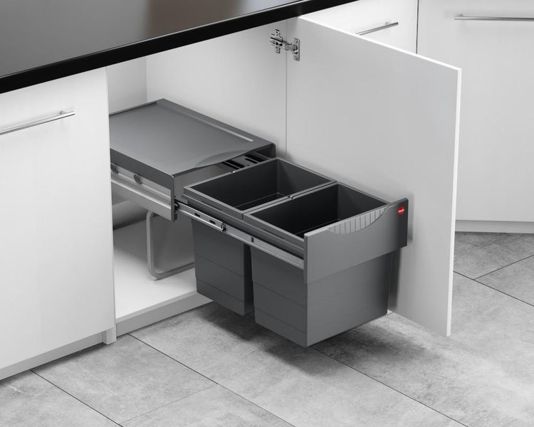 Ausziehbarer Mülleimer aus Kunststoff mit zwei Behältern zur Mülltrennung, montiert auf Metallschienen in einem organisierten Küchenunterschrank.