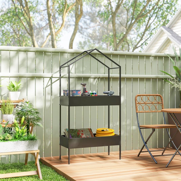 Hausförmiges Gartenregal aus Metall auf einer Holzterrasse, bestückt mit Werkzeugen, Gartenschlauch und Pflanzen in einer hellen Gartenumgebung.