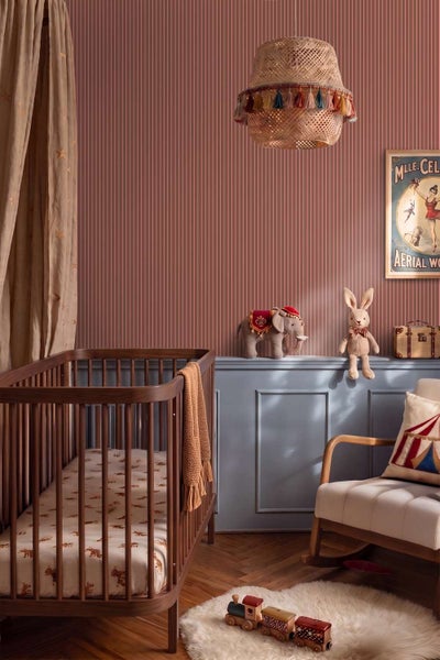 Kinderschlafzimmer mit gestreifter Tapete, Holzgitterbett, Schaukelstuhl, geflochtener Lampe mit Quasten und verspielten Zirkus Dekorationselementen.