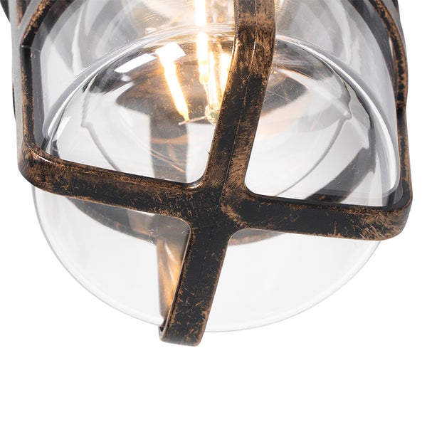 Nahaufnahme einer Außenleuchte mit Klarglas und Metallkäfig in Antik-Optik. Ein leuchtendes Leuchtmittel ist im Inneren sichtbar.