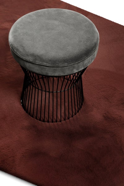 Runder Hocker mit grauem Samtsitz und schwarzem Metalldrahtgestell auf einem roten Teppich.