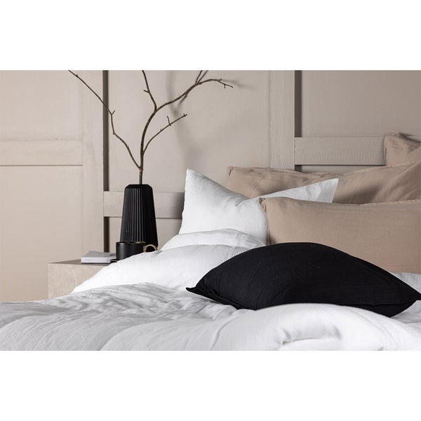 Modernes Schlafzimmer mit weißer Bettwäsche, verschiedenfarbigen Kissen und minimalistischer Dekoration auf dem Beistelltisch.