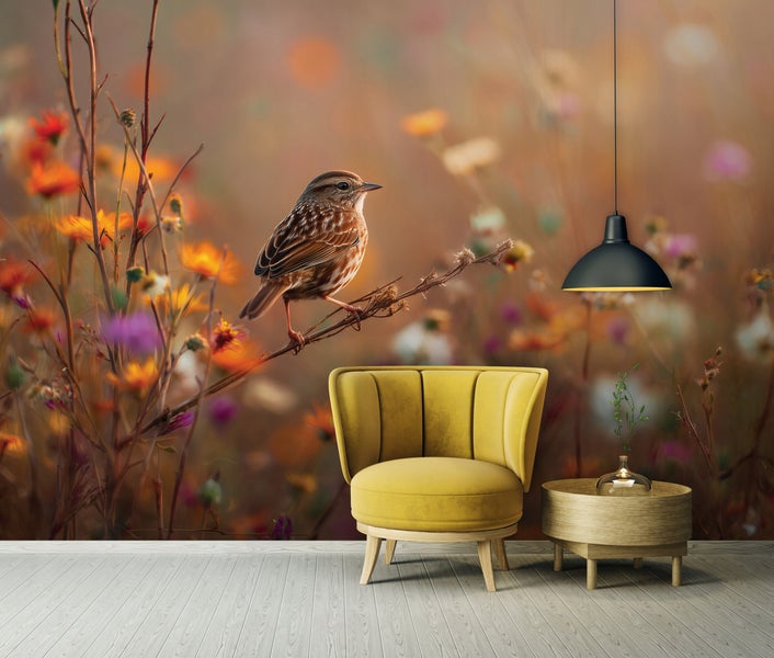 Wohnzimmer mit Vliestapete Motiv Vogel auf Zweig in Wildblumenwiese, dazu Sessel und Beistelltisch vor einer Wand mit floralem Naturmuster.