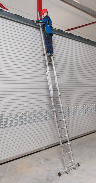 Handwerker mit Schutzhelm steht auf einer langen Aluminium Anlegeleiter an einem Industrietor.
