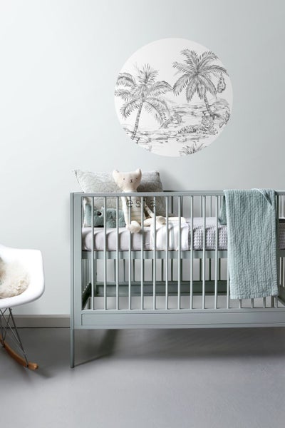 Ein Kinderzimmer mit einem Kinderbett, einem Stuhl und einem Wandbild mit Palmen.