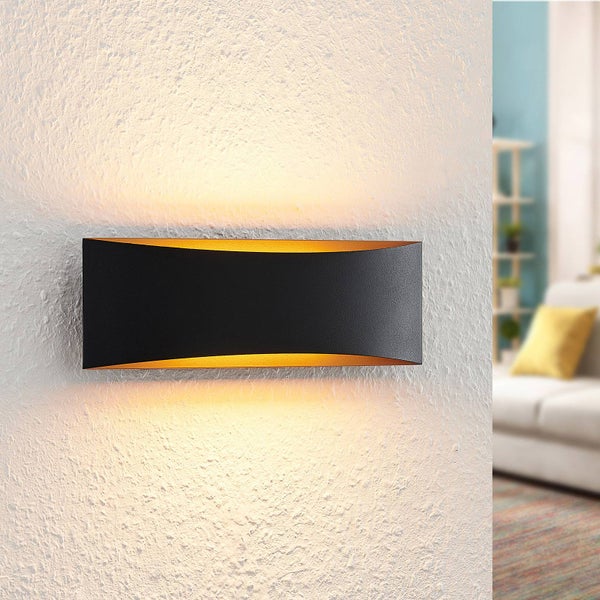 Moderne Wandleuchte in Schwarz und Gold mit Up-and-Down-Lichteffekt an einer strukturierten weißen Wand in einem hellen Wohnzimmer.