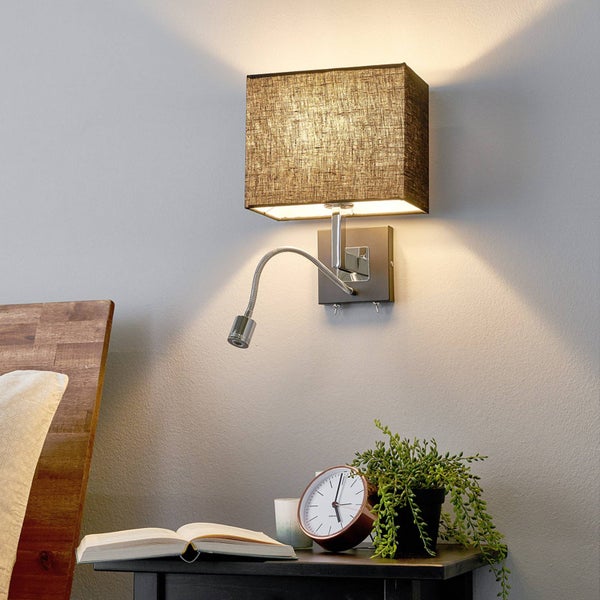 Wandleuchte mit braunem Stoffschirm und flexiblem Lesearm über einem Nachttisch mit Buch, Uhr und Pflanze.