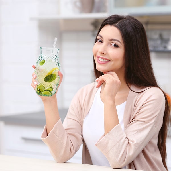 Frau hält ein Getränk mit Strohhalm in einem Glas in Ananasform