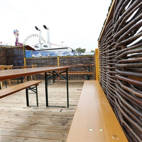 Biergartenszene mit Holztischen, Bänken und geflochtenen Wänden