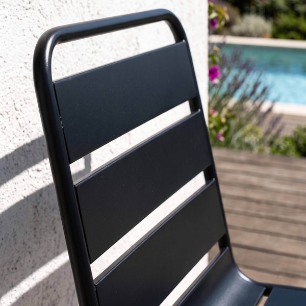 Nahaufnahme der Rückenlehne eines schwarzen Gartenstuhls aus Metall auf einer Terrasse neben einem Swimmingpool.
