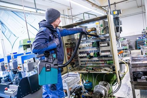 Ein Mann reinigt einen Schaltschrank mit einem Industriesauger.