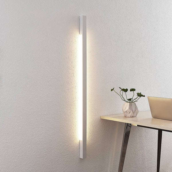 Moderne, schlanke LED-Wandleuchte in vertikaler Ausrichtung an einer strukturierten Wand neben einem organisierten Arbeitsplatz mit Schreibtisch.