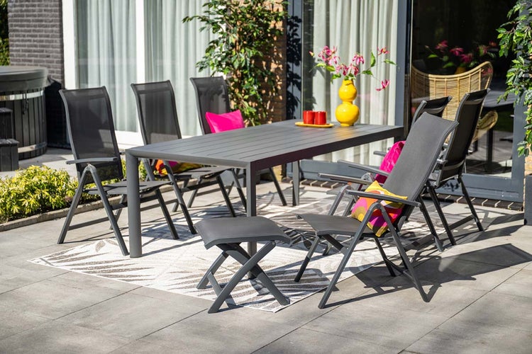 Modernes Gartenmöbel-Set aus Aluminium mit rechteckigem Tisch, klappbaren Hochlehnern und einem Hocker auf einer hellen Terrasse.