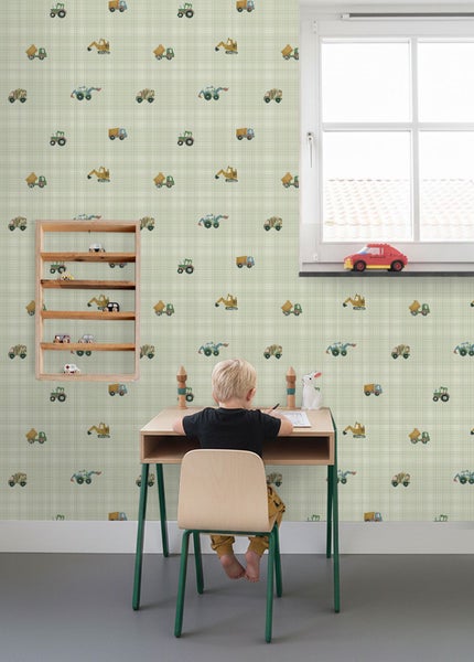 Hell eingerichtetes Kinderzimmer mit einer Vliestapete mit Karomuster und Baustellenfahrzeugen, einem Schreibtisch und einem Wandregal.