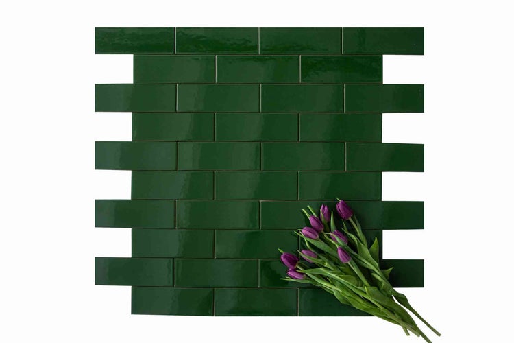 Dunkelgrüne glänzende Mosaikfliesen für die Wand im Verband verlegt mit einem Strauß lila Tulpen.