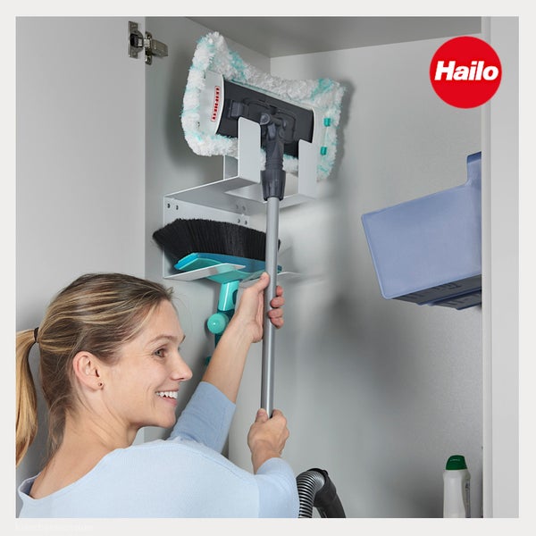 Frau verstaut Leifheit Mop und Besen in einem Hailo Ordnungssystem aus Metall in einem Schrank. Organisierte Aufbewahrung. Hailo Logo.