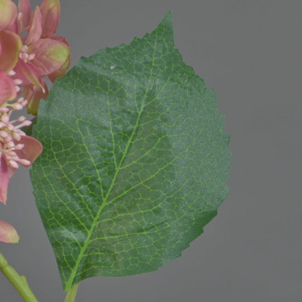 Nahaufnahme eines grünen Blattes mit gezacktem Rand und rosa Blüten einer künstlichen Blume.