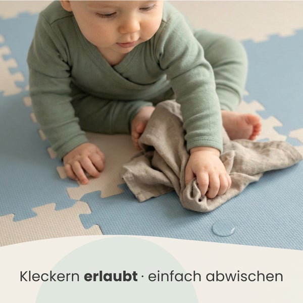 Ein Baby wischt mit einem Tuch Flüssigkeit von einer pflegeleichten Puzzlematte ab.