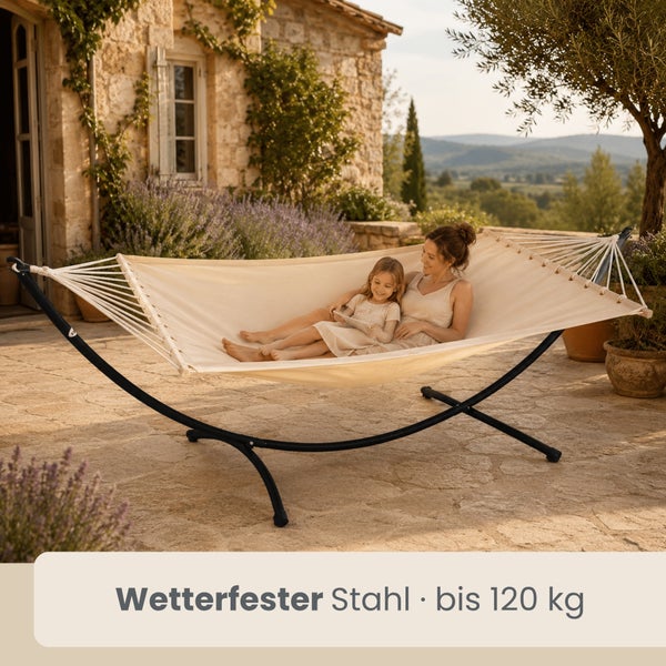 Stoffhängematte mit wetterfestem Stahlgestell bis 120 Kilogramm auf einer Steinterrasse mit Frau und Kind vor einem rustikalen Steinhaus.