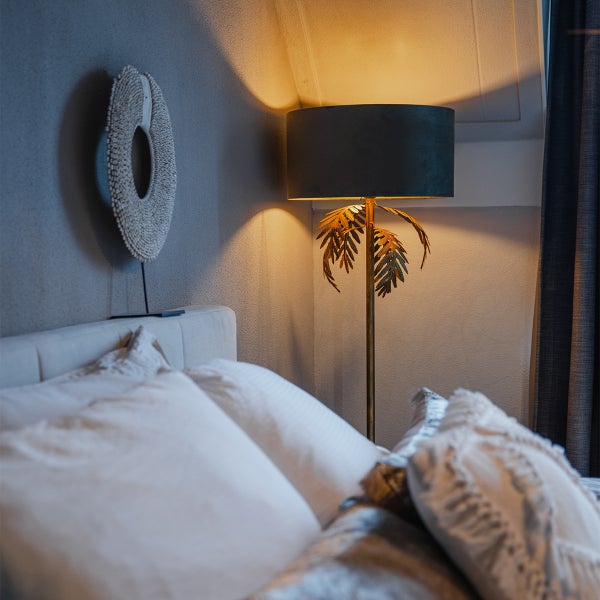 Dekoratives Schlafzimmer mit Bett, dekorativer Wandkunst und Stehlampe mit Palmenmotiv