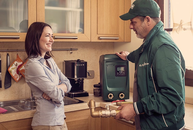 Eine Frau beobachtet einen Installateur, der eine Hauswasseranlage im Küchenbereich installiert.