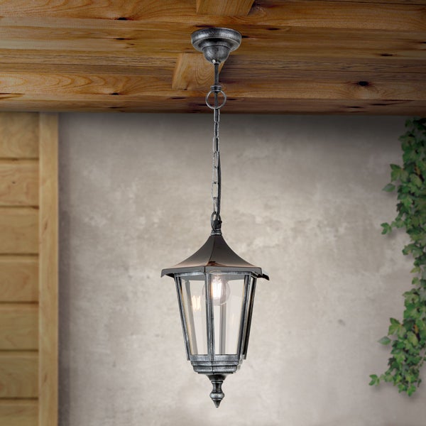 Klassische Außenpendelleuchte aus Metall und Glas mit Kette, montiert an einer Holzdecke vor einer Wand mit Kletterpflanzen.