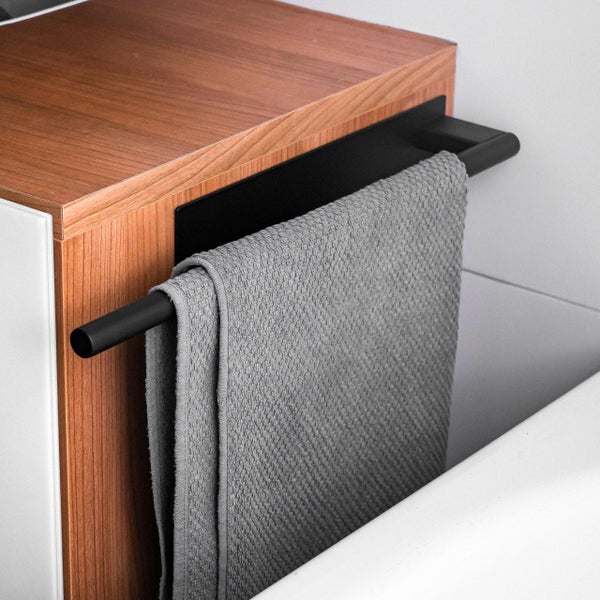 Ein schwarzer Handtuchhalter aus Metall, der seitlich an einem Badezimmerschrank mit Holzoberfläche montiert ist, mit einem hängenden Handtuch.