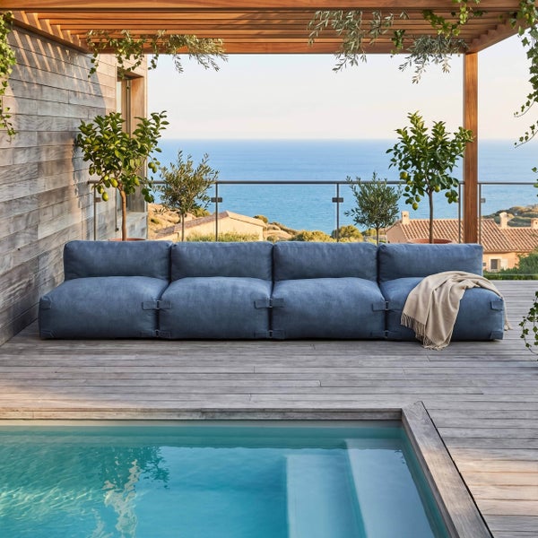 Modernes blaues Modulsofa auf einer Holzterrasse am Pool mit Meerblick und Holzpergola.