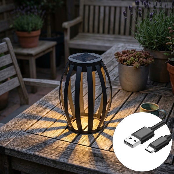 Schwarze Solar-Laterne auf einem hölzernen Gartentisch mit Ladekabel, strahlt warmweißes Licht mit dekorativem Schattenmuster aus.