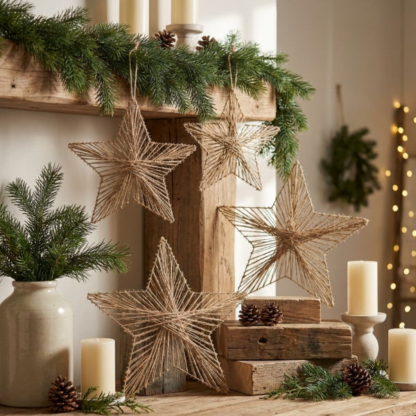 Set aus weihnachtlichen Dekosternen aus Jutegarn, dekorativ arrangiert auf einem Kamin mit Tannenzweigen, Kerzen und Zapfen für ein Festtagsambiente.