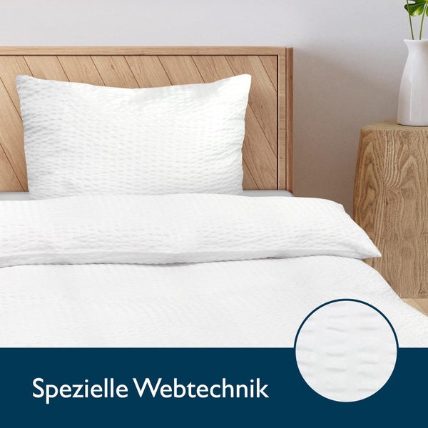 Weiße Bettwäsche mit spezieller Webtechnik auf einem Holzbett in einem hellen Schlafzimmer.