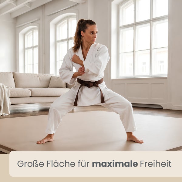 Eine Frau im Kampfsportanzug trainiert Karate auf einer großen, beigen Sportmatte in einem hellen Wohnzimmer.