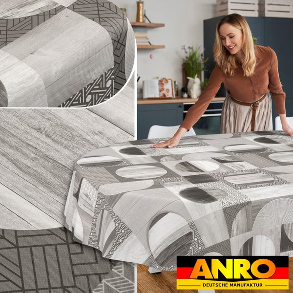 Ovale Tischdecke mit geometrischem Muster und Holzoptik auf einem Tisch in einer hellen Küche. Frau glättet den Stoff. ANRO Deutsche Manufaktur Logo.