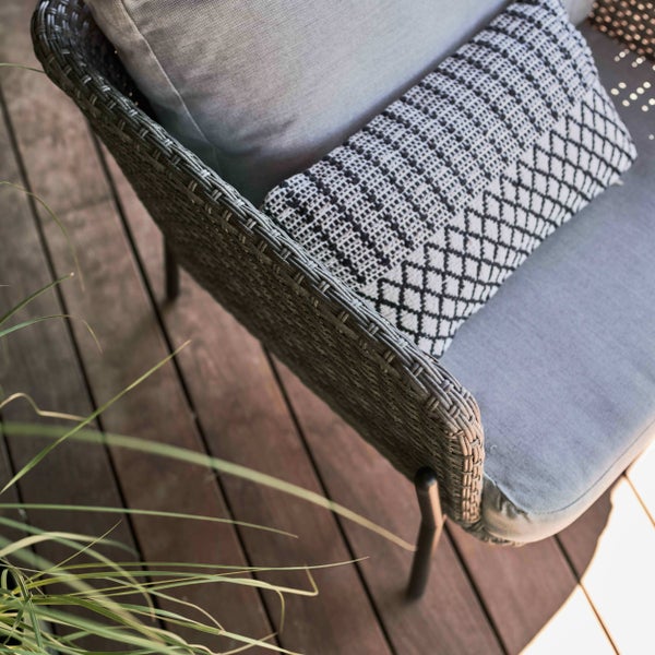 Gartenstuhl aus Polyrattan mit Sitzkissen und gemustertem Dekokissen auf einer Holzterrasse.