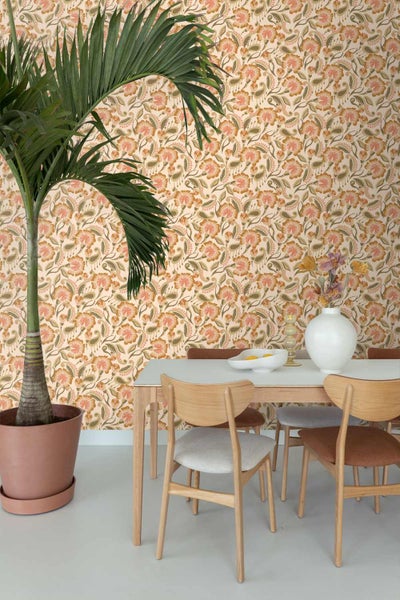 Esszimmer mit floral gemusterter Tapete, Holztisch, Stühlen und einer großen Palmenpflanze im Topf.