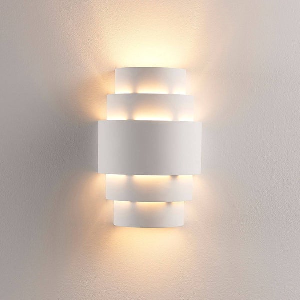 Weiße Wandleuchte mit gestuftem, mehrschichtigem Design und warmem Lichtschein nach oben und unten.