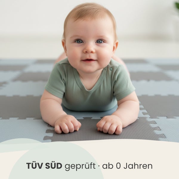 Baby liegt auf einer TÜV SÜD geprüften Puzzlematte, geeignet für Kinder ab null Jahren.