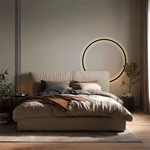Modernes Schlafzimmer mit gepolstertem Bett, Textilbettwäsche und einer großen, kreisförmigen LED-Wandleuchte für stimmungsvolles Licht.