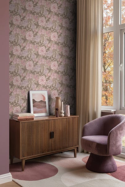 Wohnraumszene mit floraler Tapete in Rosa und Braun. Ein Sideboard aus Holz, ein lila Sessel und Vorhänge schaffen ein warmes Ambiente.