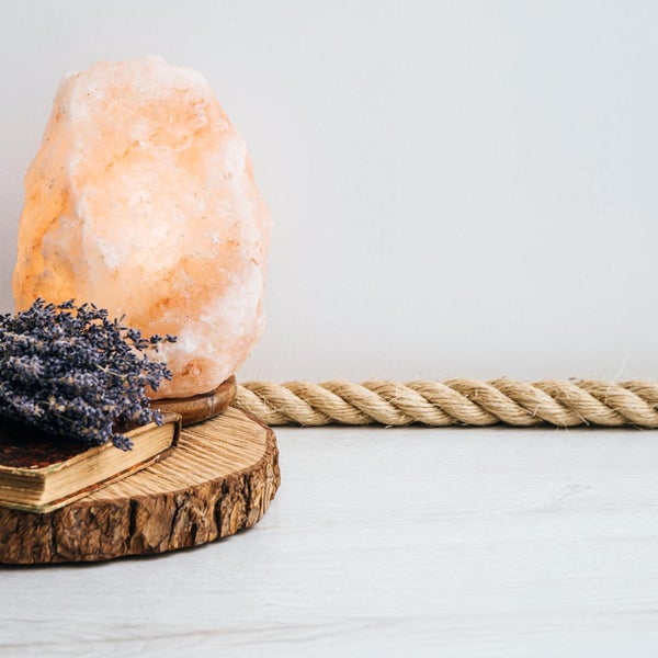 Beleuchtete Salzlampe auf einer Baumscheibe neben getrocknetem Lavendel und einem Buch, im Hintergrund ein dickes Seil auf hellem Holzboden.