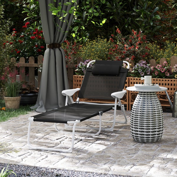 Moderne Gartenliege mit weißem Metallgestell und schwarzer Textilbespannung auf Steinterrasse. Daneben runder Beistelltisch in geflochtener Optik.