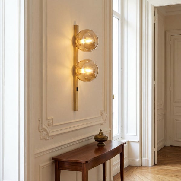 Wandleuchte aus Messing mit zwei Glaskugeln an einer Wand mit Zierleisten in einem klassisch eingerichteten Raum.