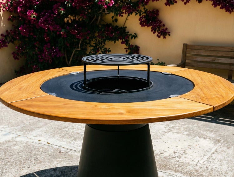 Runder Holztisch mit integrierter Feuerschale und Grillrost auf einer Terrasse.