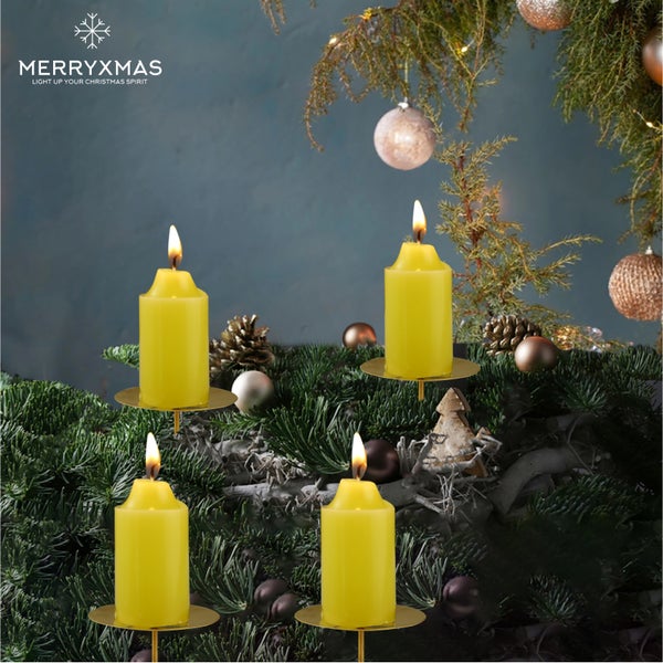 Gesteck mit vier gelben Stumpenkerzen auf goldenen Kerzenhaltern, kombiniert mit Tannengrün und Weihnachtskugeln.